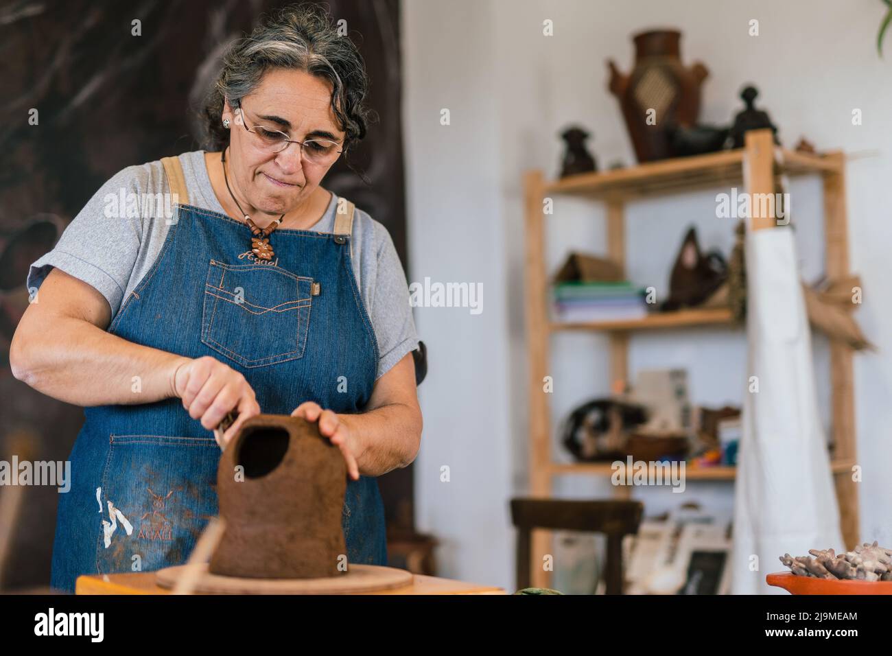 Femme mature Cramamiste Woman en tablier en utilisant l'outil et en créant le modèle sur pot d'argile dans l'atelier Banque D'Images
