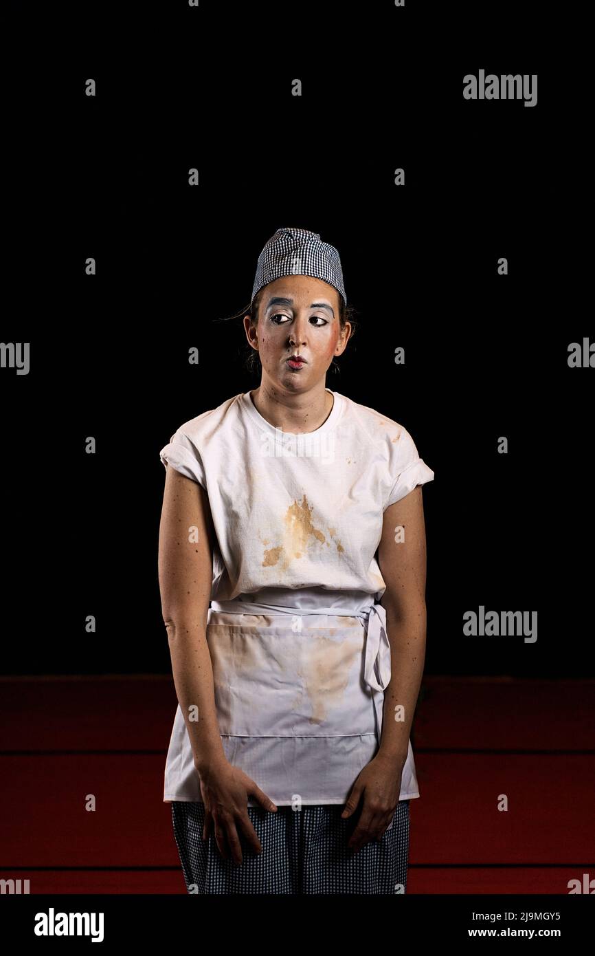 Drôle jeune femme mime artiste avec maquillage dans la maison sale vêtements faisant le visage et regardant loin sur fond noir Banque D'Images