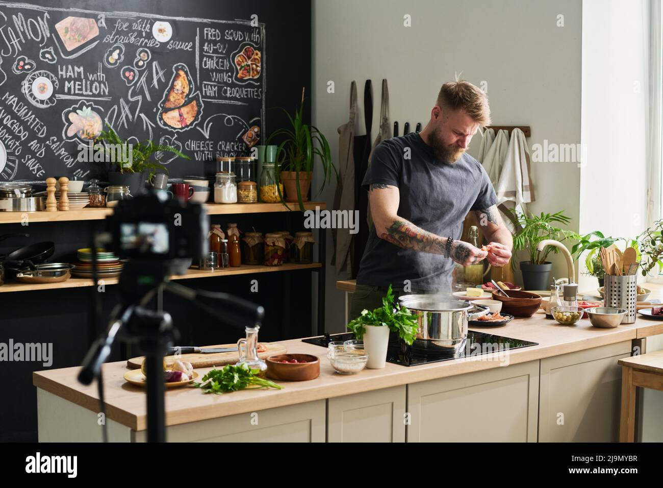 Beau blogueur de nourriture barbu debout dans la cuisine loft cuisine cuisine repas sur appareil photo Pehmps peeling Banque D'Images