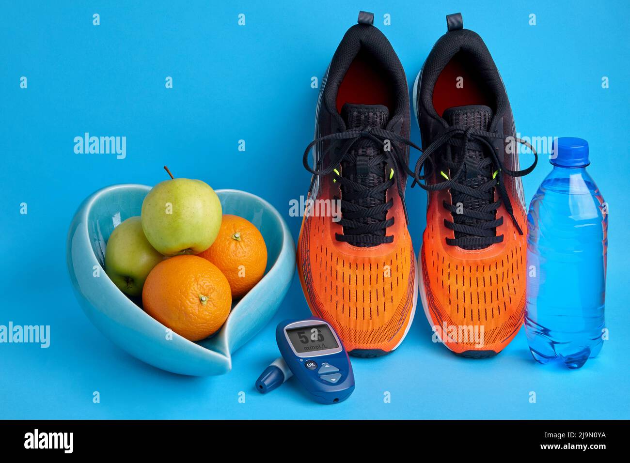 Baskets, fruits dans un bol en forme de coeur et bouteille d'eau sur fond bleu Banque D'Images