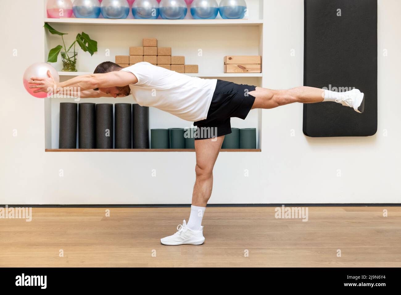 Vue latérale d'un athlète musclé de sexe masculin dans l'équilibre de sportswear sur la jambe et l'exercice avec medecine ball rempli de fluide dans le centre de fitness Banque D'Images