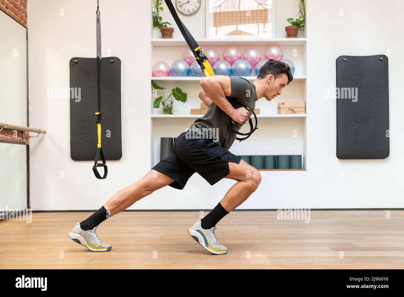 Vue latérale de l'homme sportif ciblé dans les vêtements de sport faisant des exercices sur les cordes TRX pendant l'entraînement en suspension dans le club de fitness spacieux Banque D'Images
