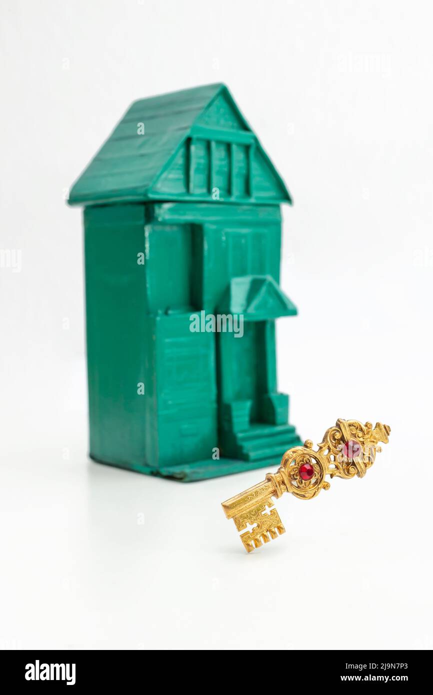 Clé dorée vintage lévitant devant une maison verte défocuée, isolée sur fond blanc Banque D'Images
