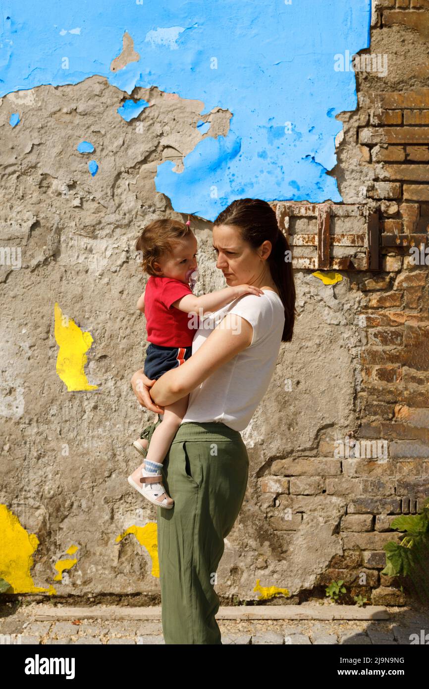 Une femme tenant son enfant devant une vieille façade dévastée Banque D'Images