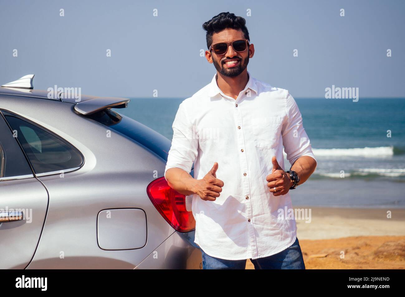 Homme d'affaires indien debout près de la voiture à l'extérieur sur la plage de mer été bon jour.un homme dans une chemise blanche et neige-blanc sourire se réjouissant d'acheter une nouvelle voiture Banque D'Images