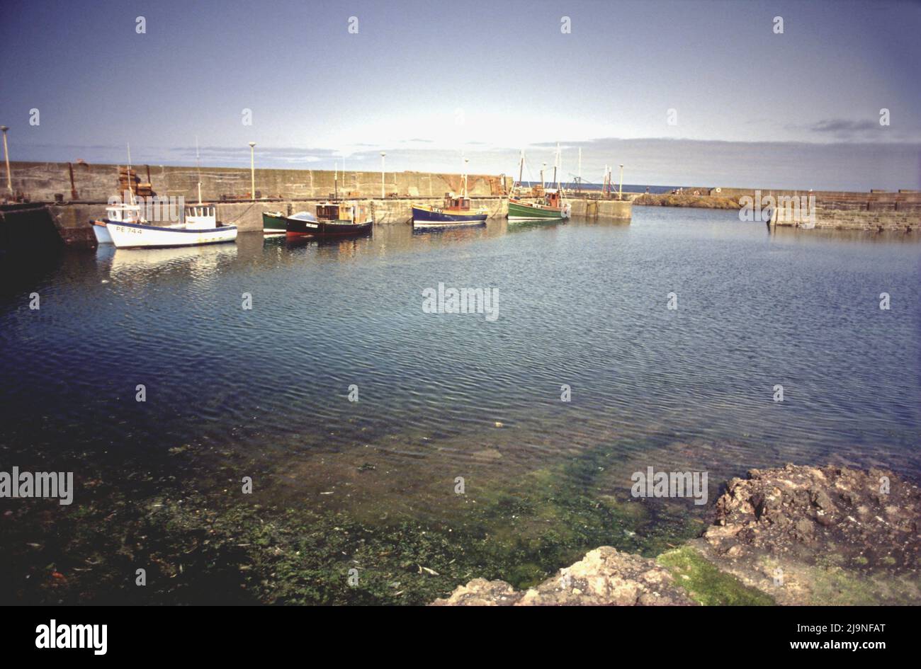 Port de St Abbs, marée haute avec bateaux de pêche attachés contre le mur du port. Jour ensoleillé, blanc, bleu, bateaux de pêche verts, Royaume-Uni des années 90 Banque D'Images