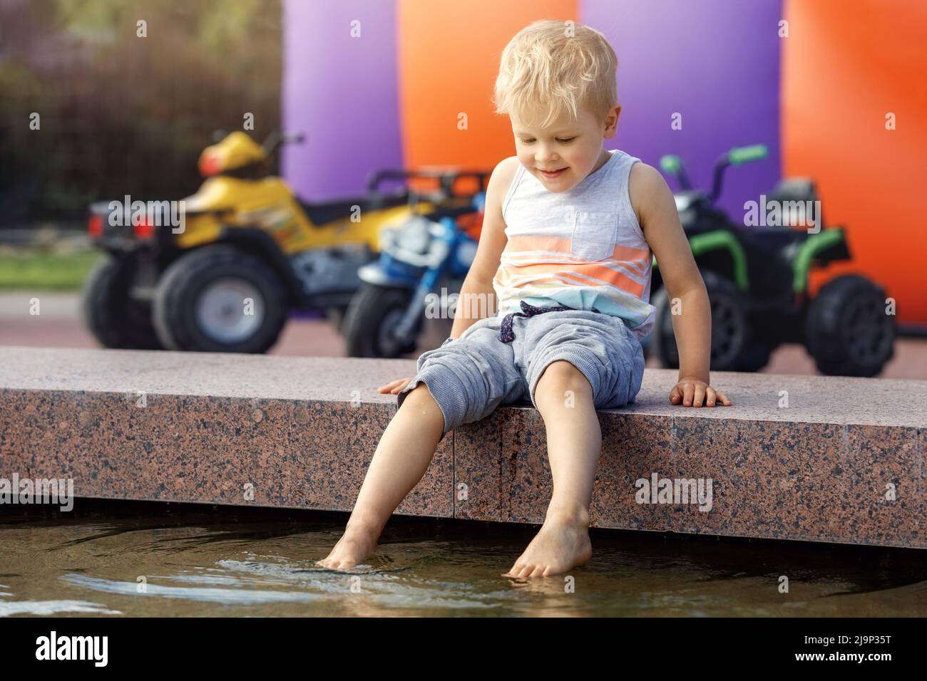Un petit garçon joue et rafraîchit les pieds dans l'eau de fontaine lors d'une chaude journée d'été. Banque D'Images