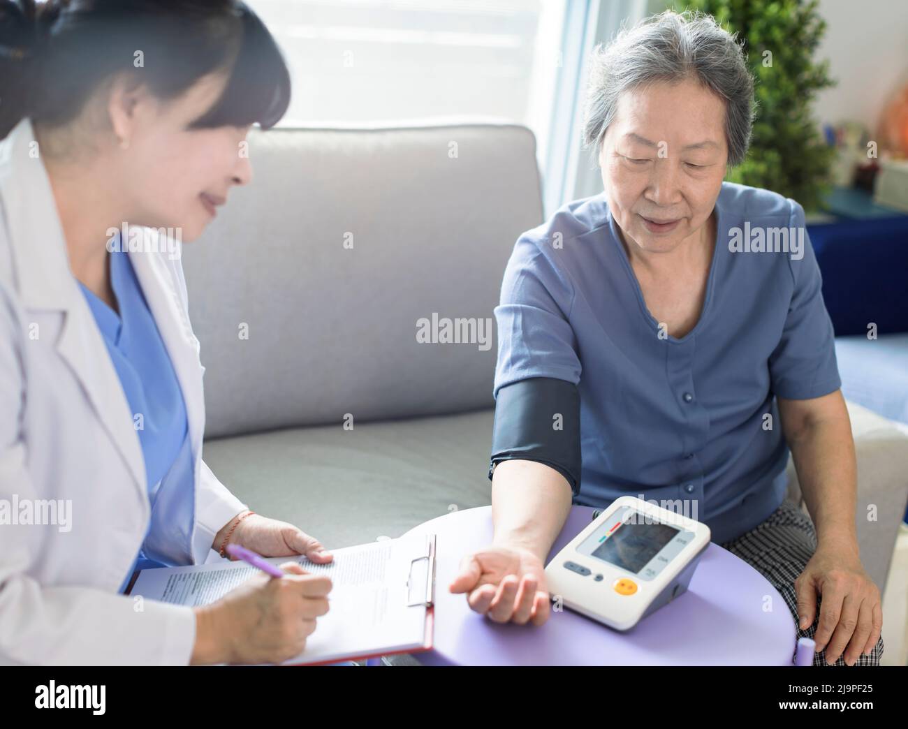 Un médecin soignant asiatique examine les patients âgés qui utilisent un manomètre de pression artérielle. Banque D'Images