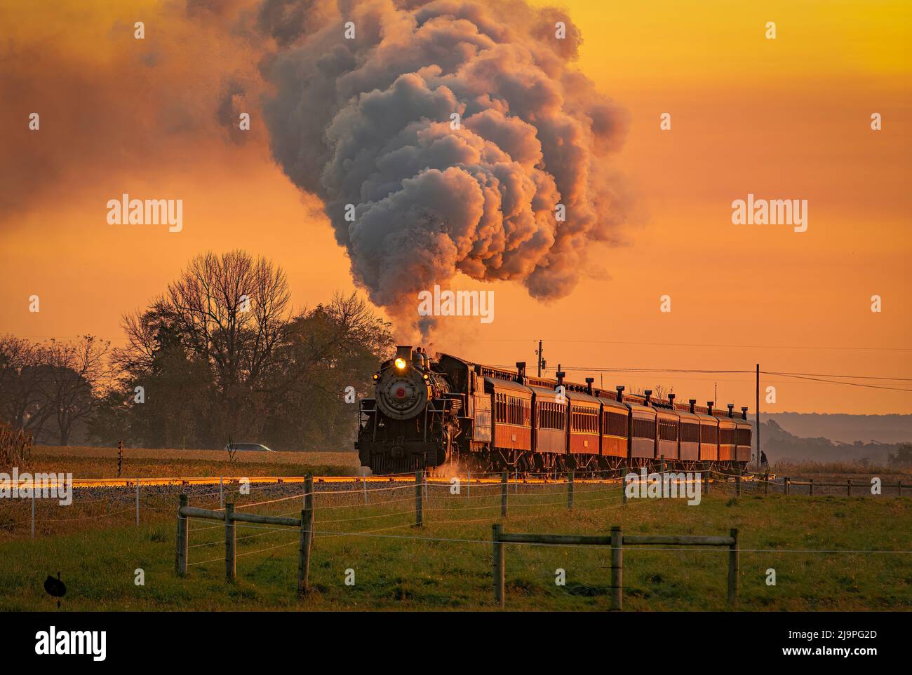 Vue sur un train de passagers à vapeur antique qui s'approche à Sunrise avec une tête de vapeur et de fumée qui se déplace à travers les terres agricoles Banque D'Images