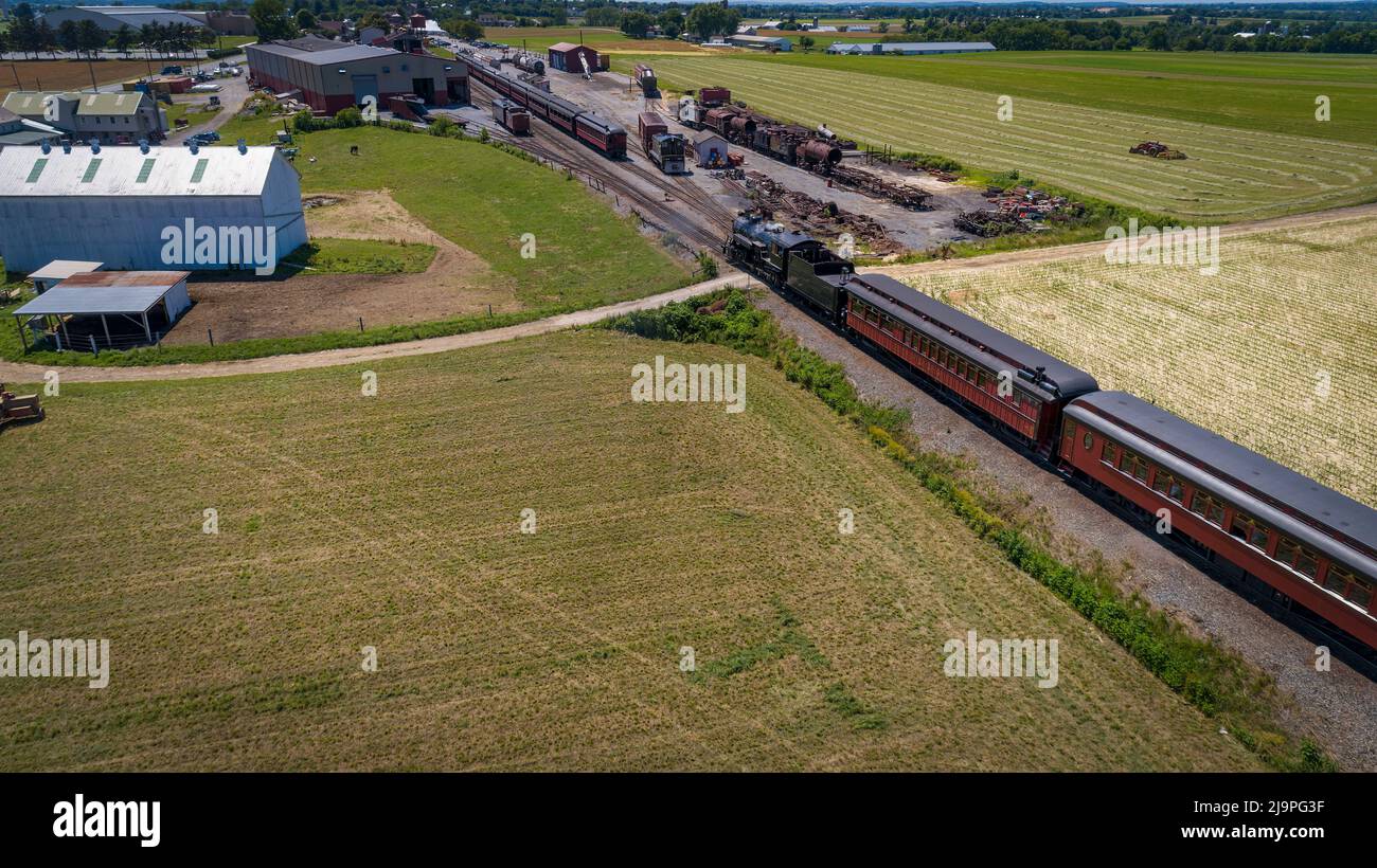 Vue aérienne depuis l'arrière d'un train de passagers à vapeur en direction de sa gare à travers les champs de cultures fraîchement récoltées lors d'une Sunny journée d'été Banque D'Images