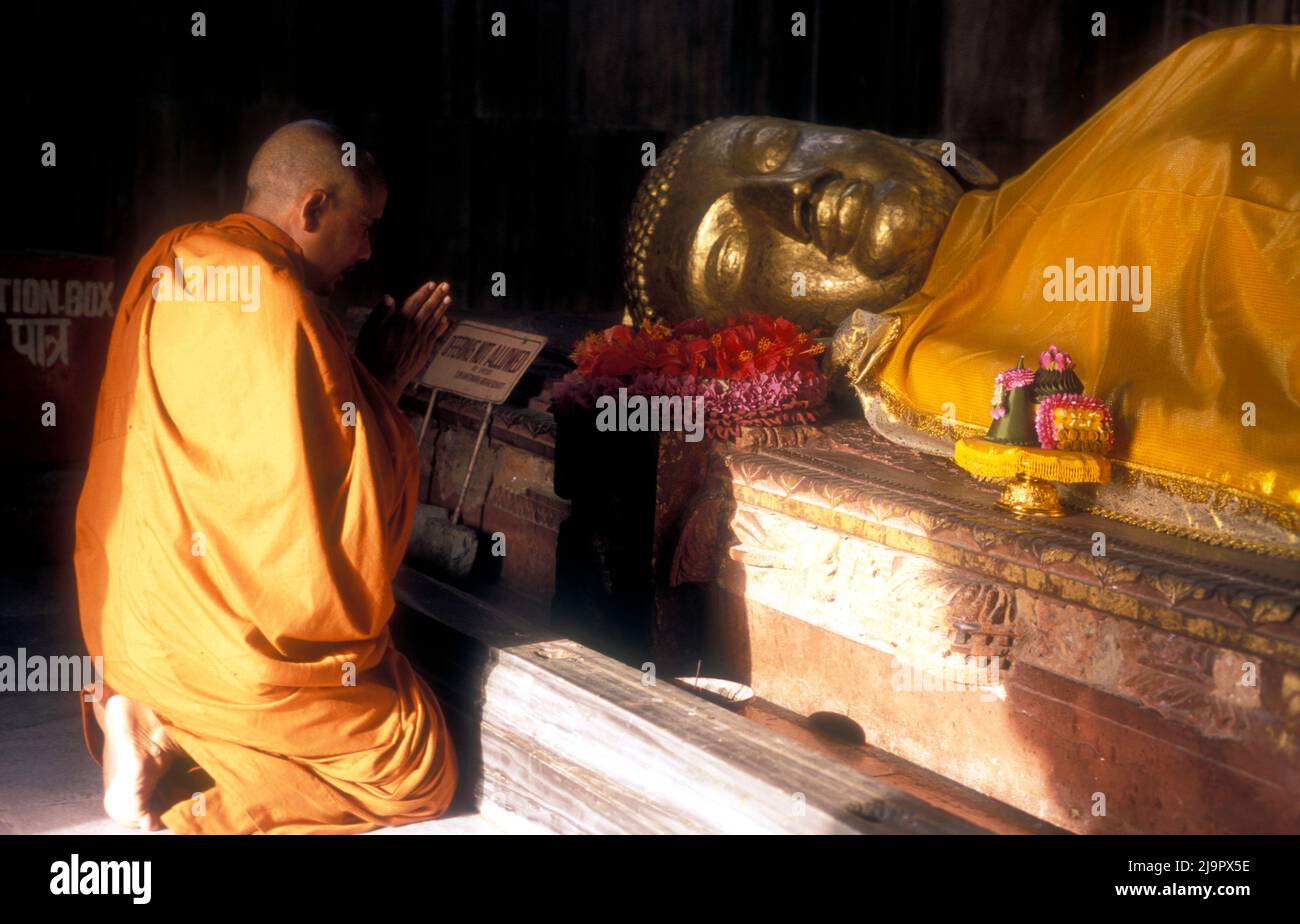 Un moine prie sous une statue du Bouddha mort, Koushinagar, lieu bouddhiste de pèlerinage en Inde. Banque D'Images