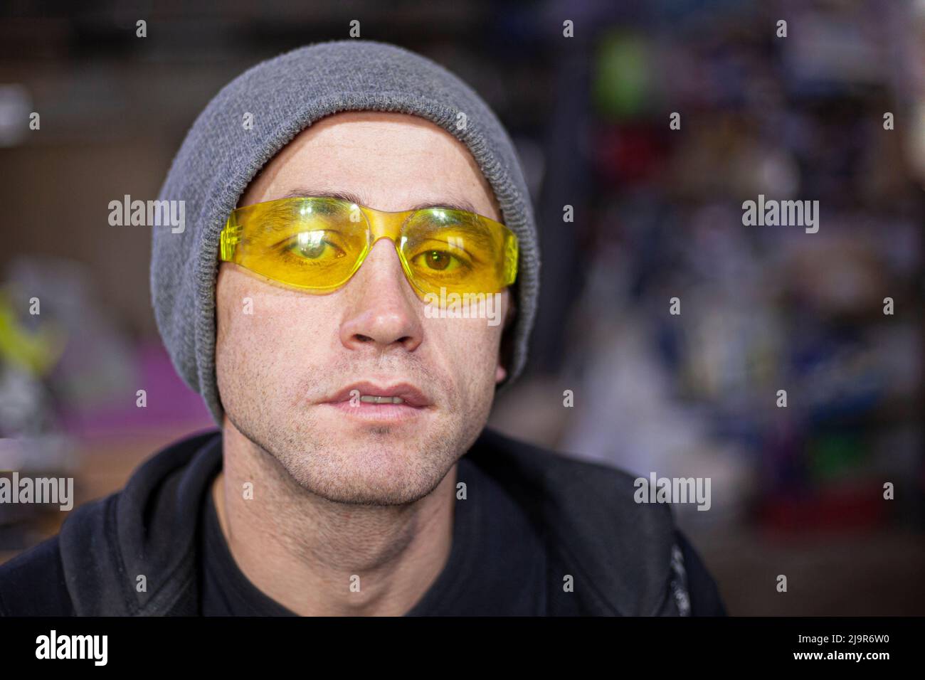 Le gars dans les verres jaunes. Portrait d'un homme en lunettes de sécurité dans un atelier. Portrait en éclairage artificiel. Jeune homme au travail. Type européen de Banque D'Images