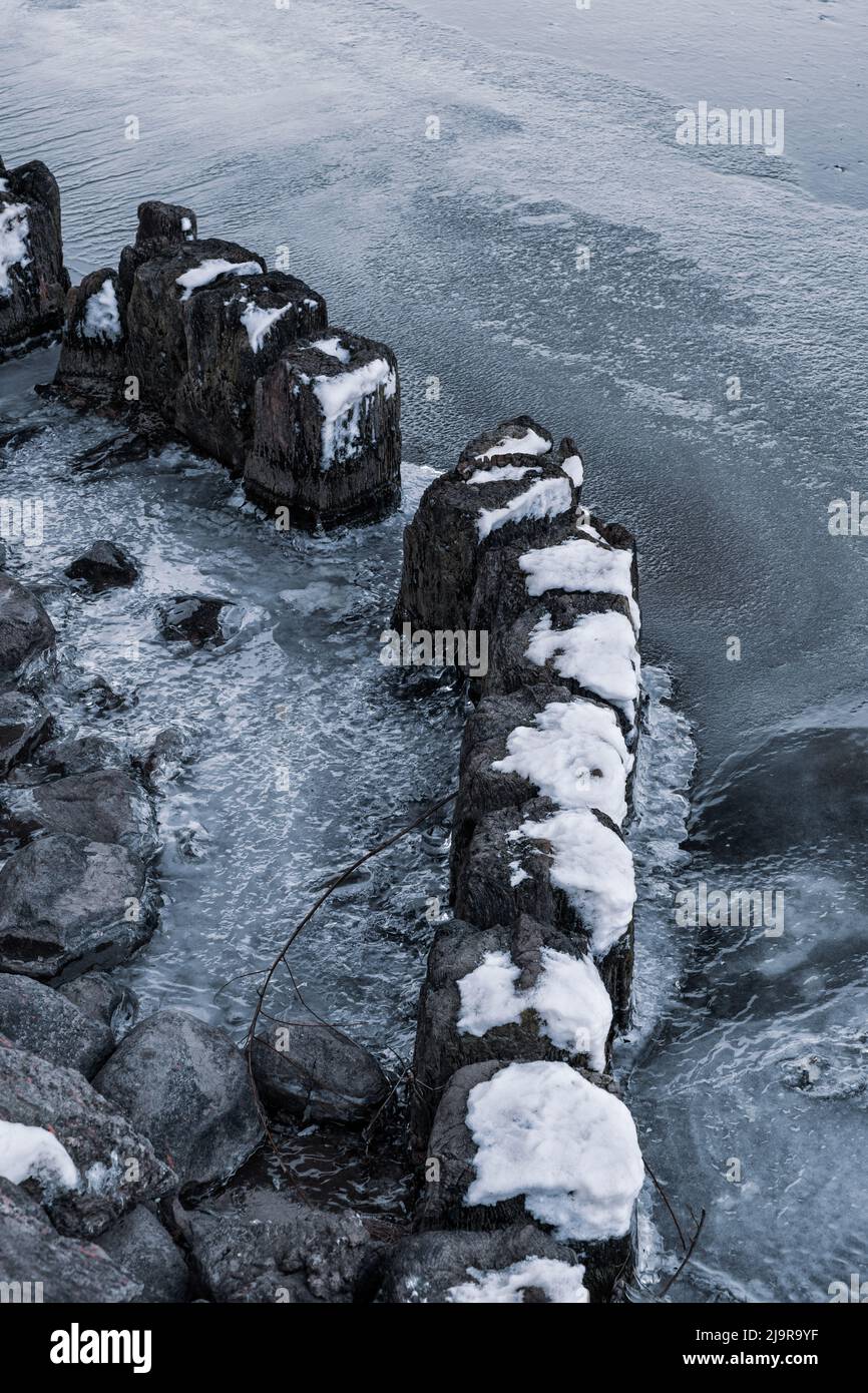 Vieux poteaux en bois avec des chapeaux de neige dans la rivière gelée à l'aube froide de la saison d'hiver. Banque D'Images