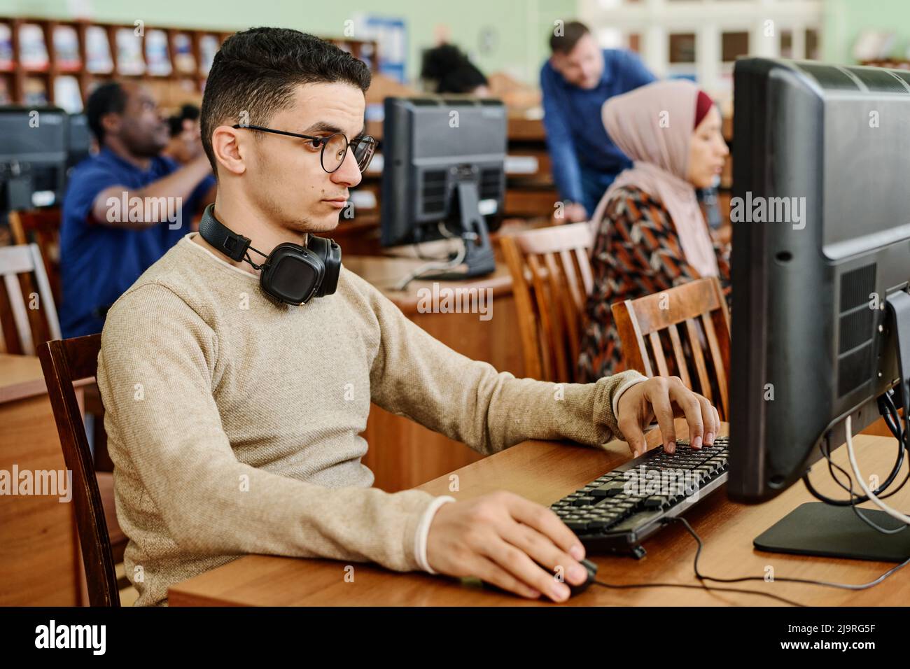 Groupe d'étudiants ethniquement divers assis dans une bibliothèque universitaire moderne travaillant sur des ordinateurs Banque D'Images