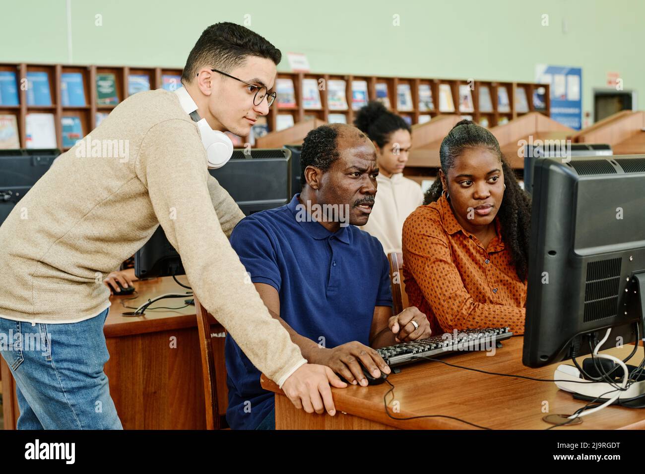 Groupe de trois étudiants migrants recherchant des données sur Internet sur un ordinateur de bureau dans une bibliothèque universitaire Banque D'Images