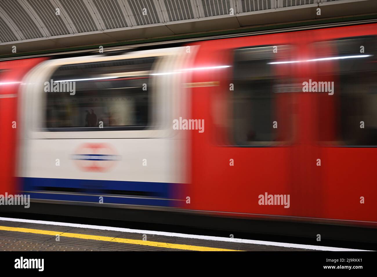 Une photo à vitesse d'obturation lente d'un train souterrain de Londres passant par la plate-forme stationnaire, montrant le mouvement du train de métro. Banque D'Images