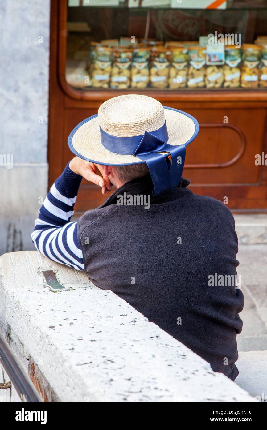Italie, Venise. Entraîneur de gondole avec chemise à rayures bleues et blanches et chapeau avec ruban bleu. Banque D'Images