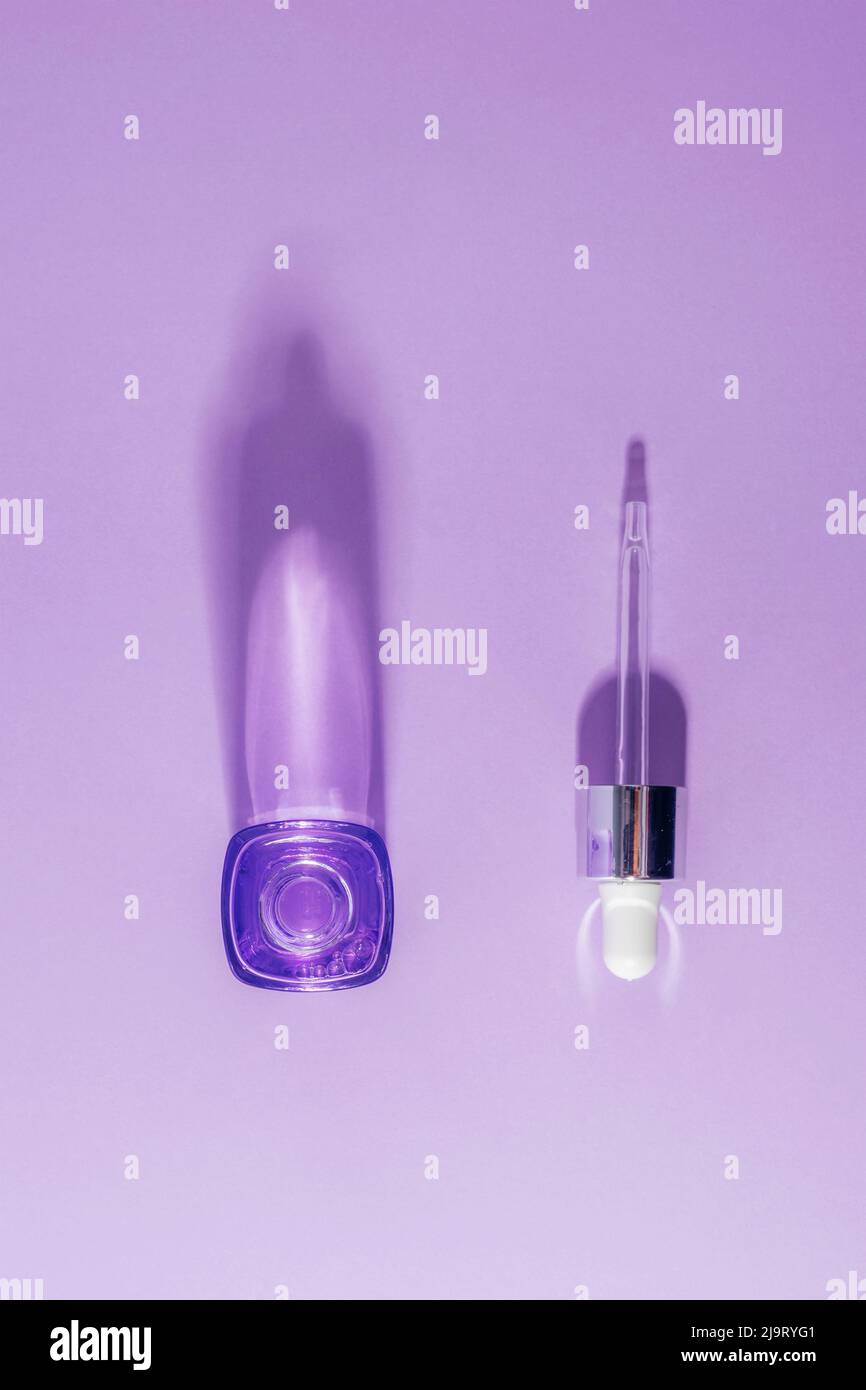 Sérum cosmétique avec compte-gouttes sur fond violet. Concept de soins de la peau. Ombres dures. Vue de dessus, plan d'appartement. Banque D'Images