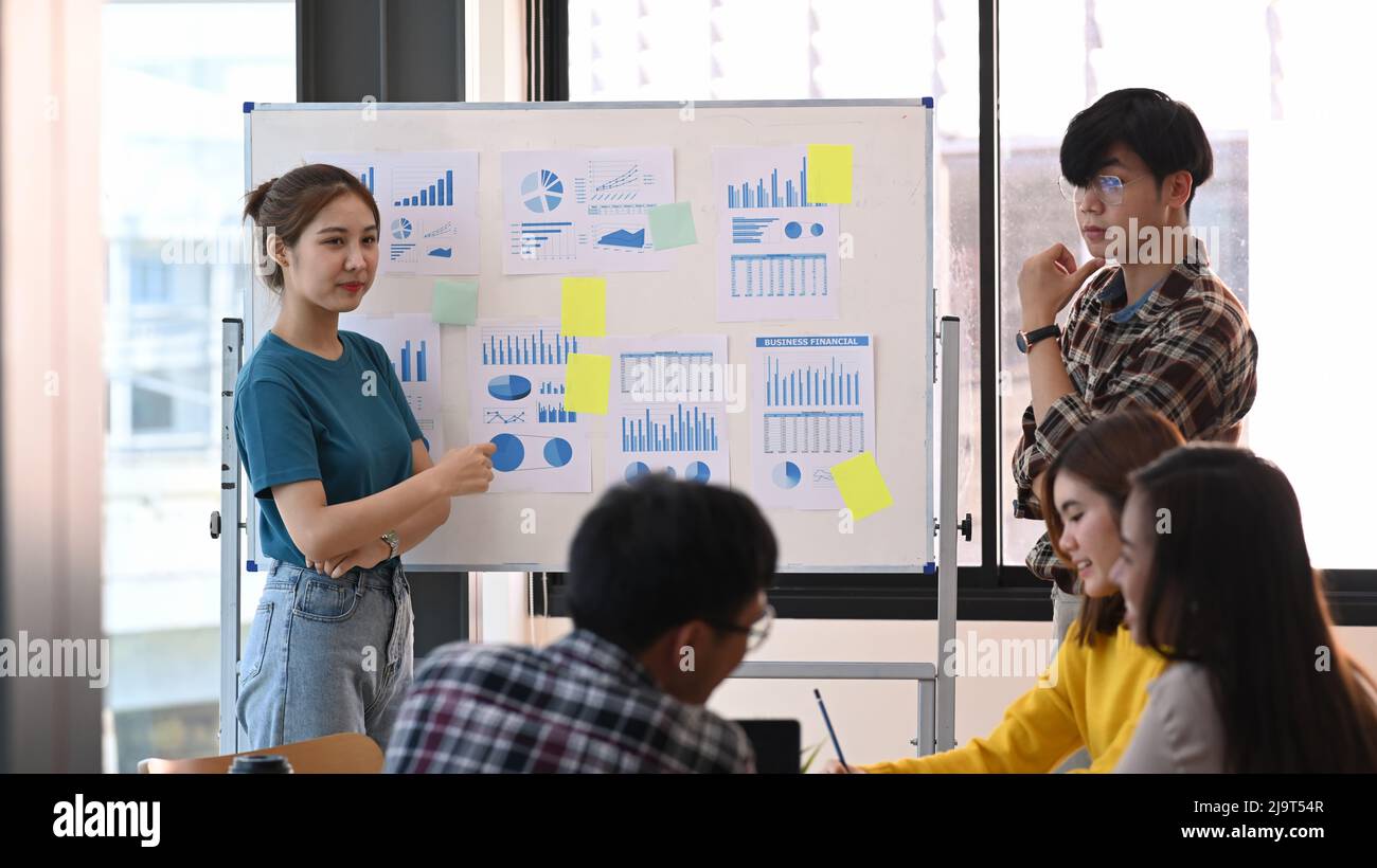 Femme confiante se tenant près du tableau de conférence avec son collègue et donnant la présentation de la nouvelle stratégie de marketing. Banque D'Images