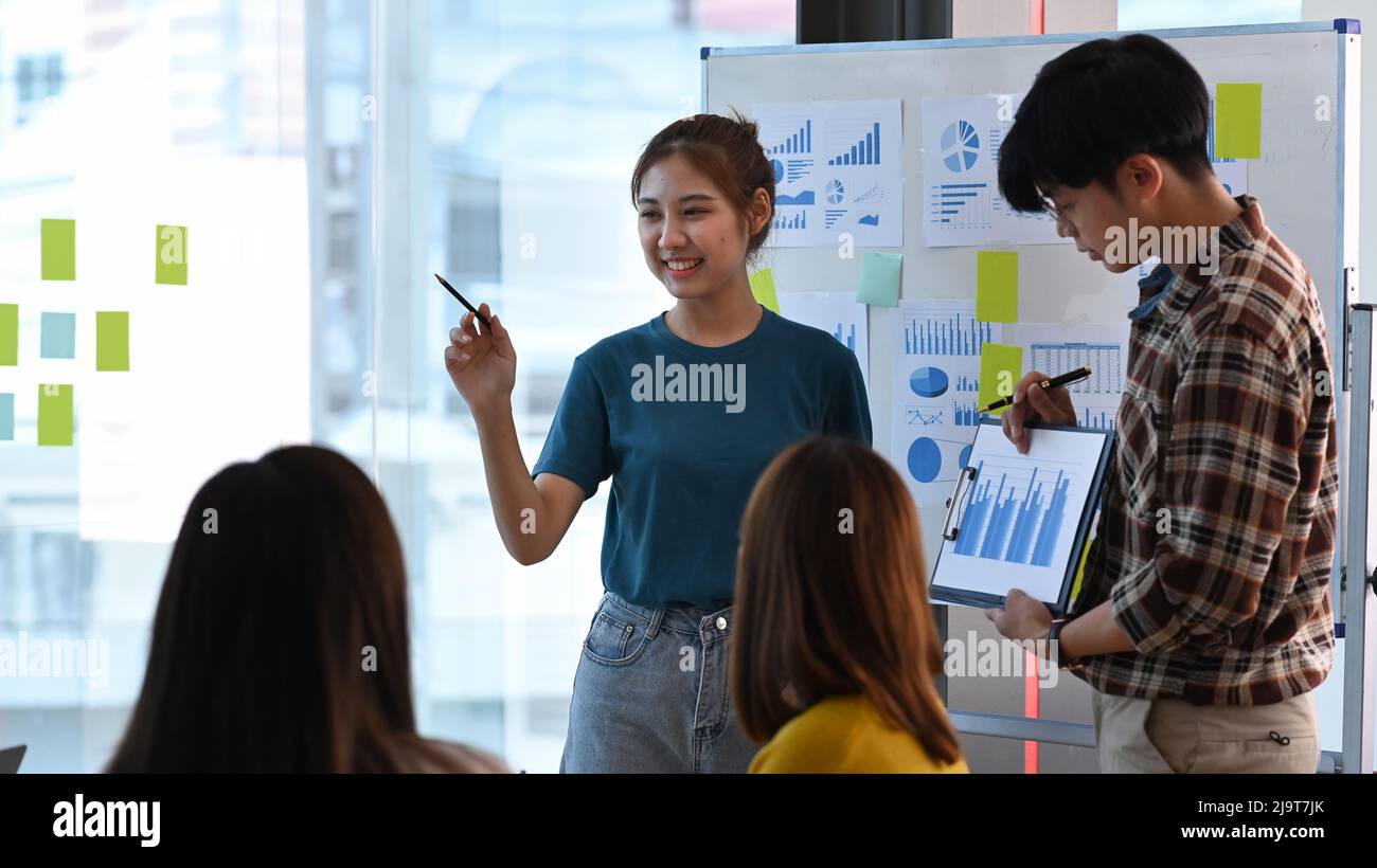 Jeune femme créative se tenant près du tableau de conférence avec son collègue et donnant la présentation de la nouvelle stratégie de marketing au bureau. Banque D'Images