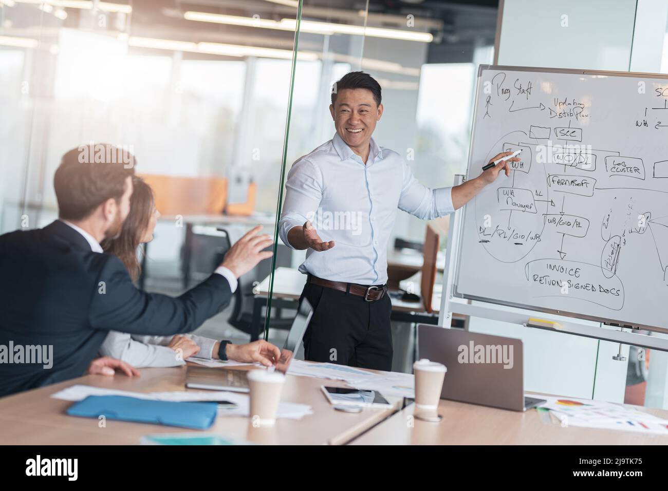 Un coach ou un conférencier asiatique mature fait une présentation du tableau de conférence à divers hommes d'affaires lors d'une réunion Banque D'Images