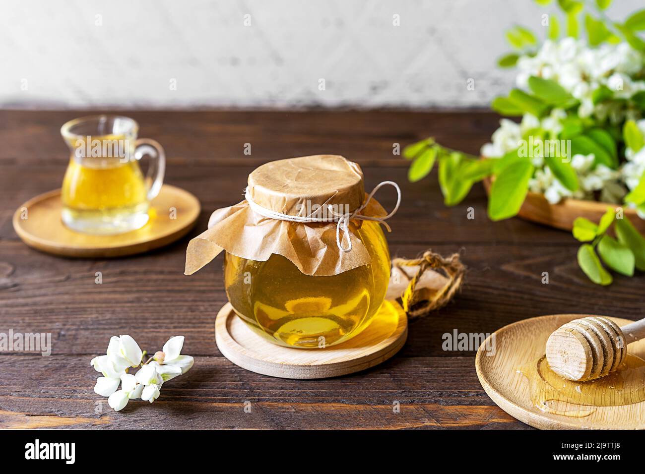 Miel d'acacia dans un pot en verre avec des fleurs de côté sur fond de bois Banque D'Images