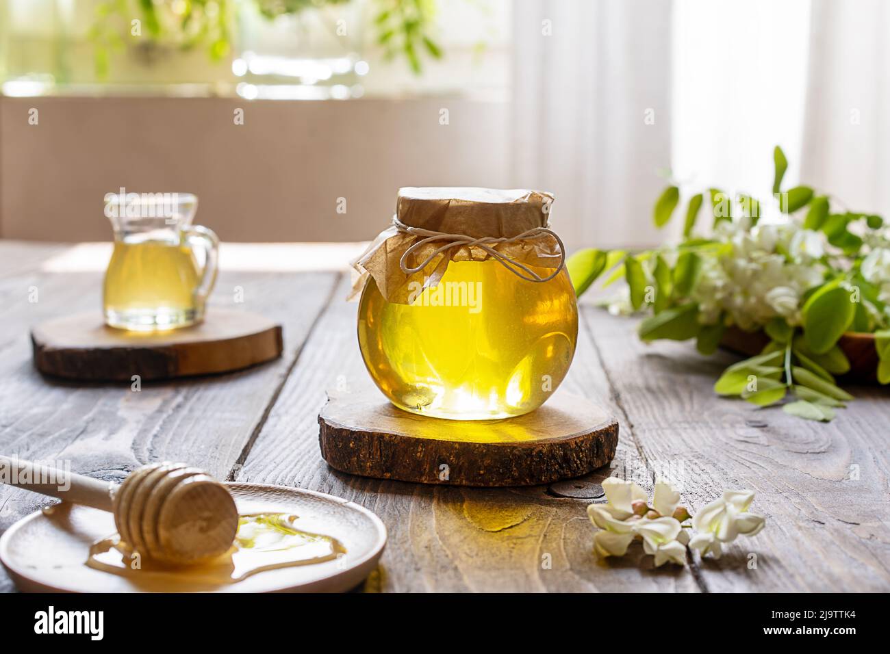 Miel d'acacia dans un pot en verre avec un balancier en bois et des fleurs de côté sur fond en bois Banque D'Images