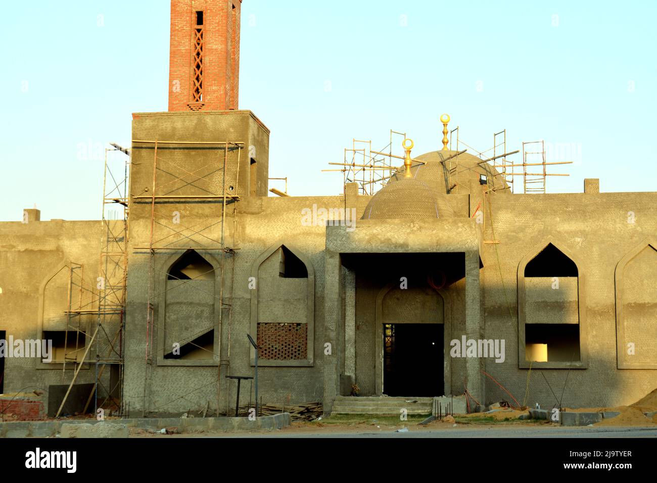 Une nouvelle mosquée est en construction contre le ciel bleu ensoleillé avec le minaret de la mosquée et les dômes entourés d'un échafaudage en bois et de fenêtres sous const Banque D'Images
