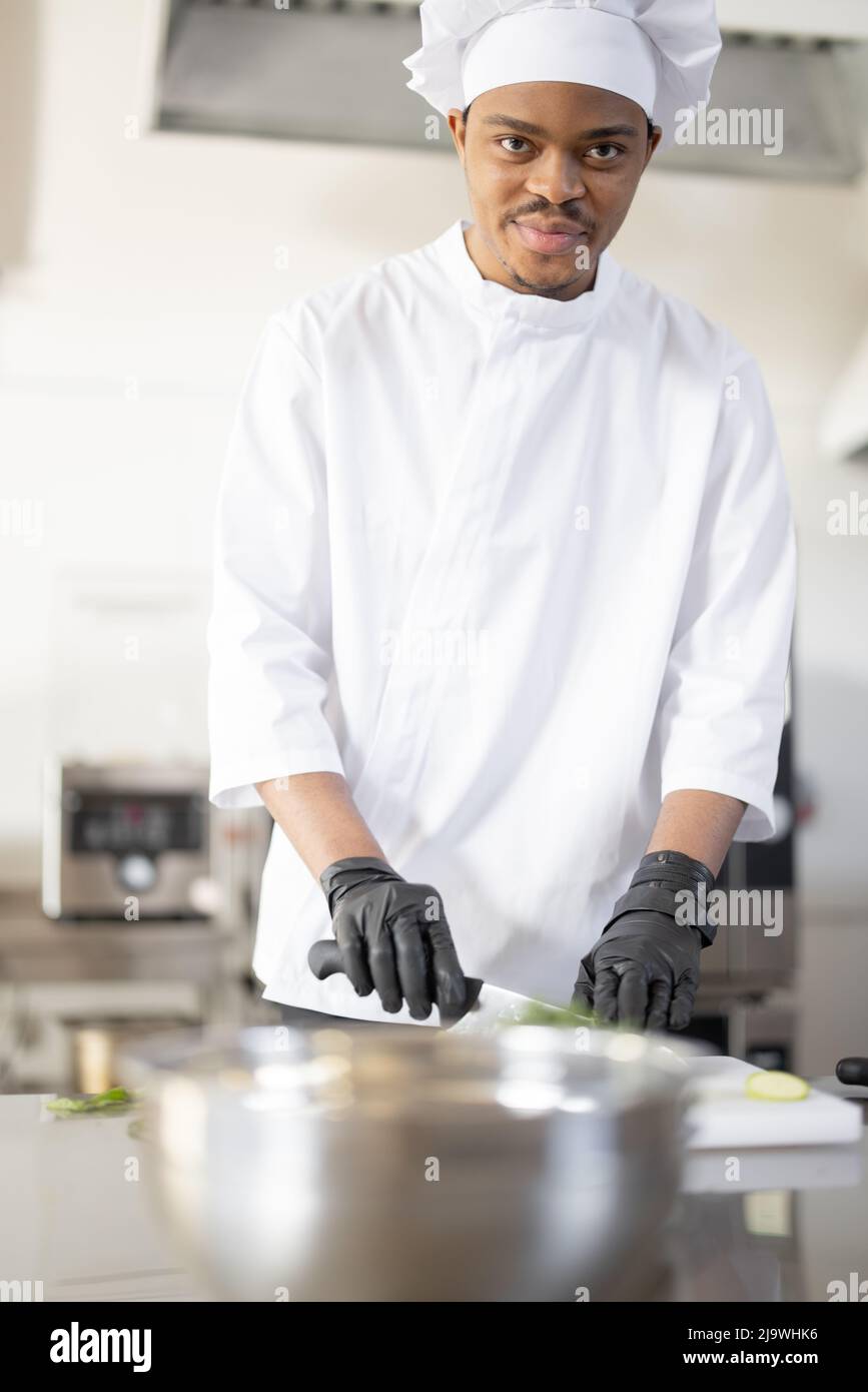 Portrait d'un jeune chef latino-américain cuisiné en uniforme dans la cuisine professionnelle. Un homme charmant qui travaille comme cuisinier au restaurant Banque D'Images