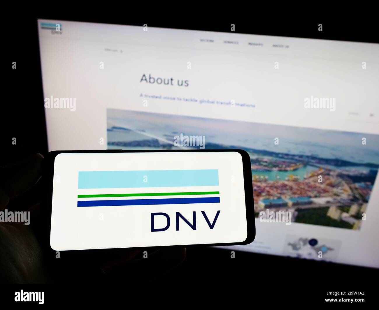 Personne tenant un smartphone avec le logo de la société norvégienne de services DNV COMME sur l'écran devant le site Web. Mise au point sur l'affichage du téléphone. Banque D'Images