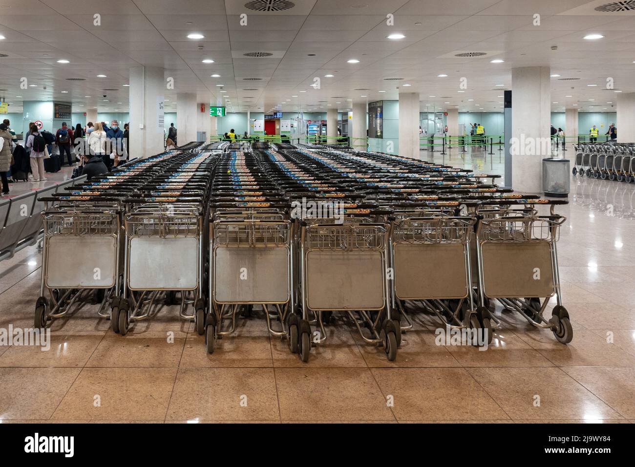 Barcelone, Espagne - 15 avril 2022 - vue sur de nombreux chariots à bagages vides empilés dans une rangée dans le hall de l'aéroport avec des passagers attendant Banque D'Images