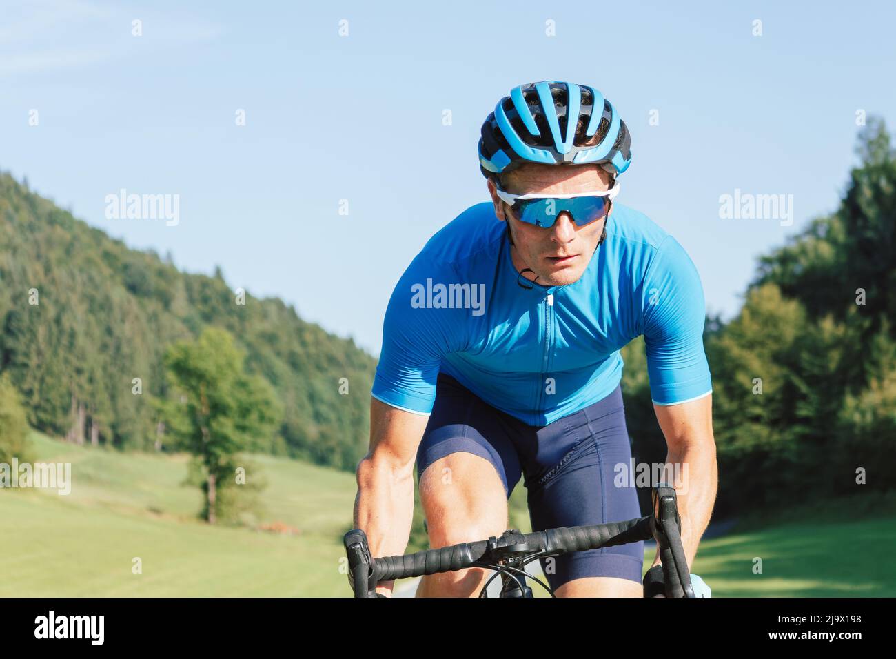 Athlète homme en maillot bleu et en équipement de vélo, en train de monter un cycle de course professionnel sur la route pavée Banque D'Images