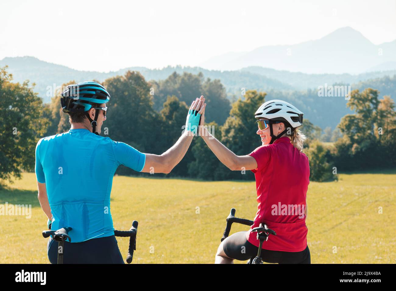Femme et homme sur des cycles de course sur route prenant une pause après un entraînement réussi et regardant le coucher de soleil sur les montagnes donnant élevé cinq Banque D'Images