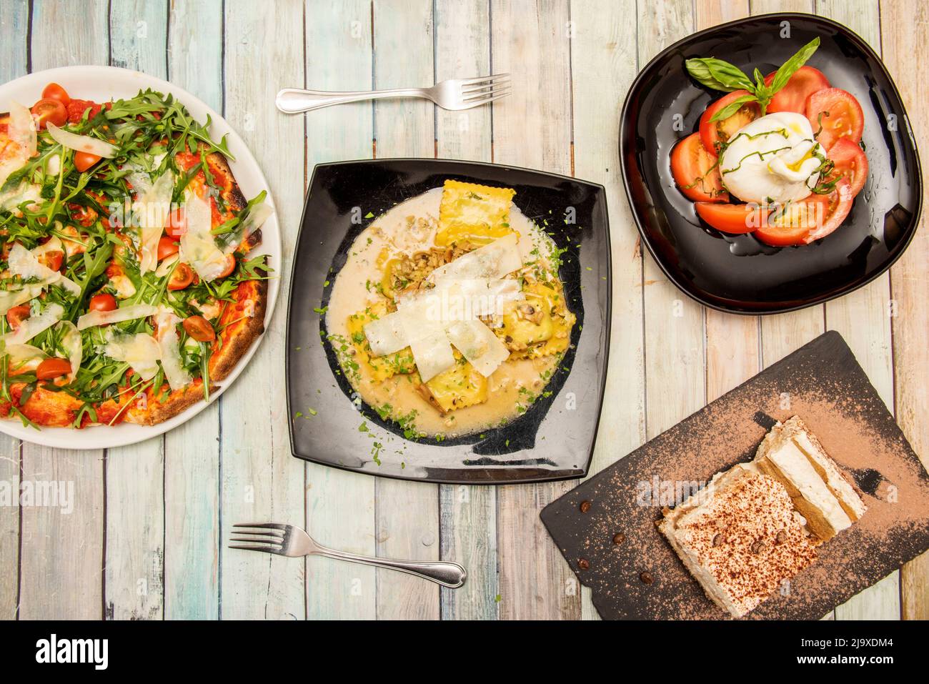 Plats italiens avec pâtes, salade burrata avec tomates et huile d'olive et pizza napolitaine avec arugula, parmesan, tomates cerises et tirami Banque D'Images