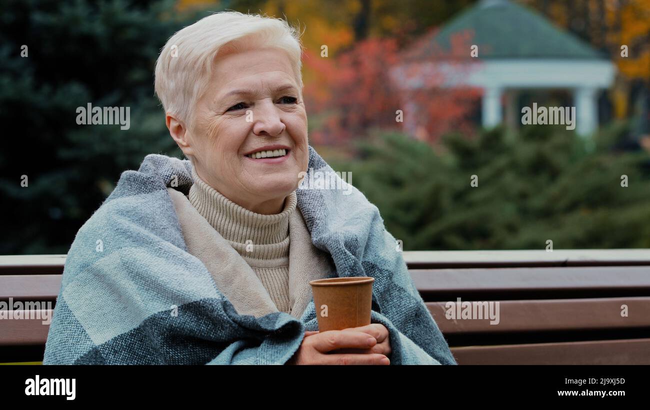 Bonne mature célibataire femme d'âge moyen couverte de chaud à boire du café chaud jetable tasse saine gai pensionné senior appréciant le repos Banque D'Images