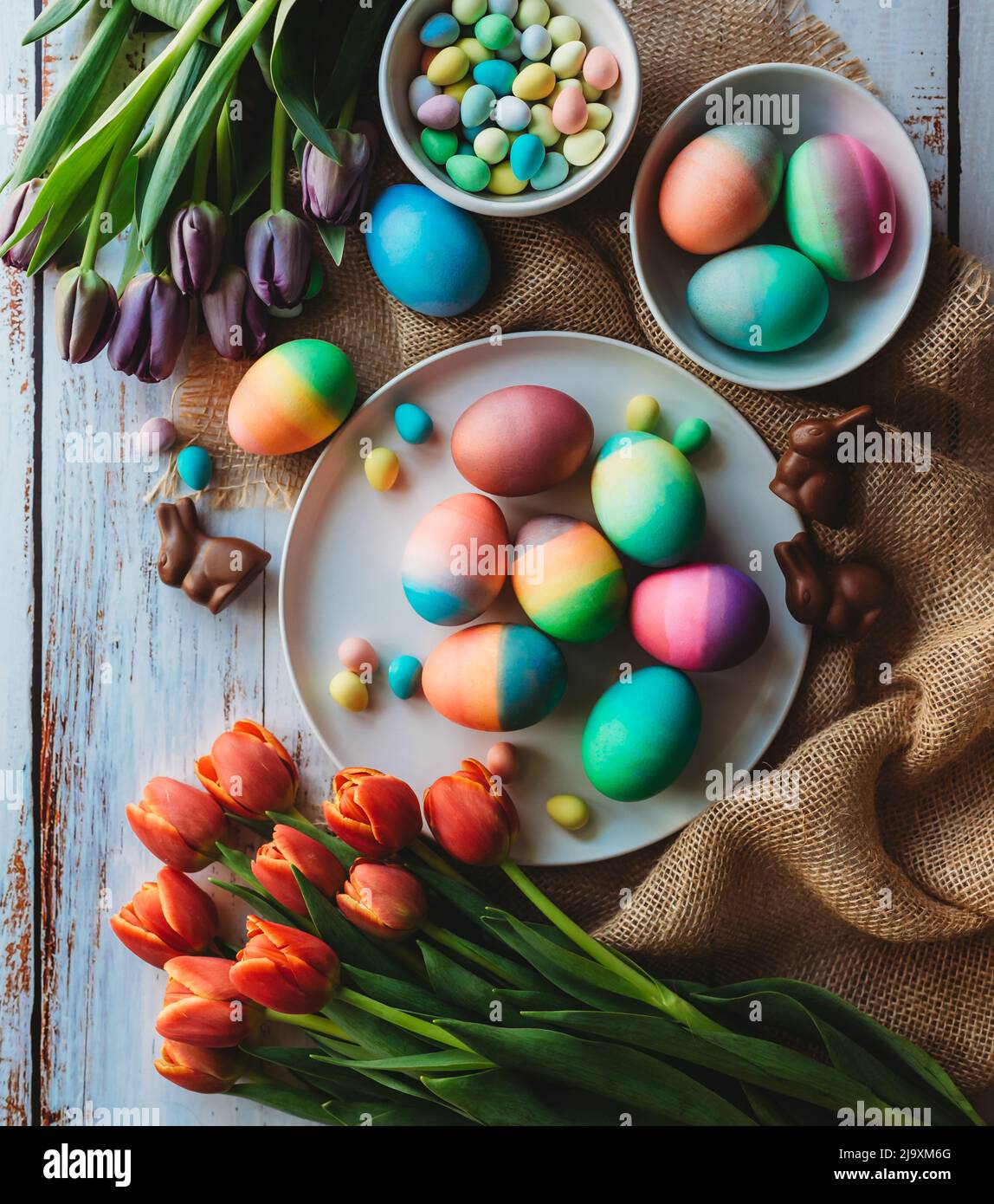 Assortiment d'œufs de pâques aux couleurs vives entourés de tulipes. Banque D'Images