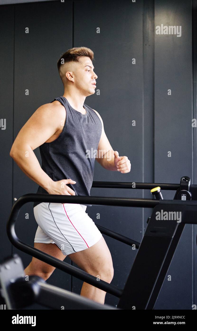 Homme dans les vêtements de sport courir sur le tapis roulant tout en s'entraîner dans la salle de gym. Banque D'Images