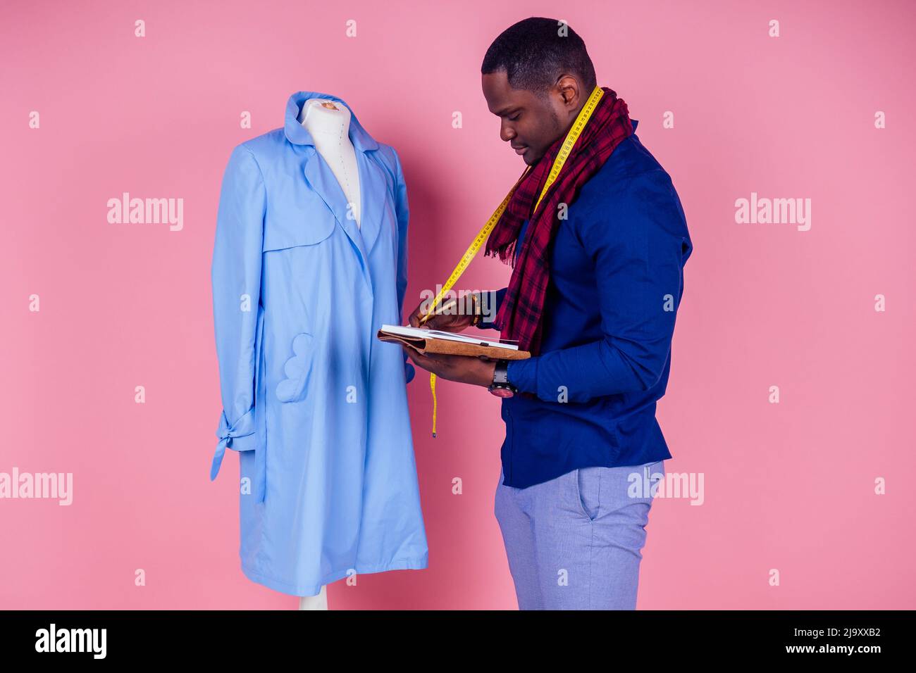 Un homme américain travaillant dans un atelier sur mesure rade un manteau bleu sur fond rose.jeune designer de mode africain avec mannequin au studio de couture Banque D'Images