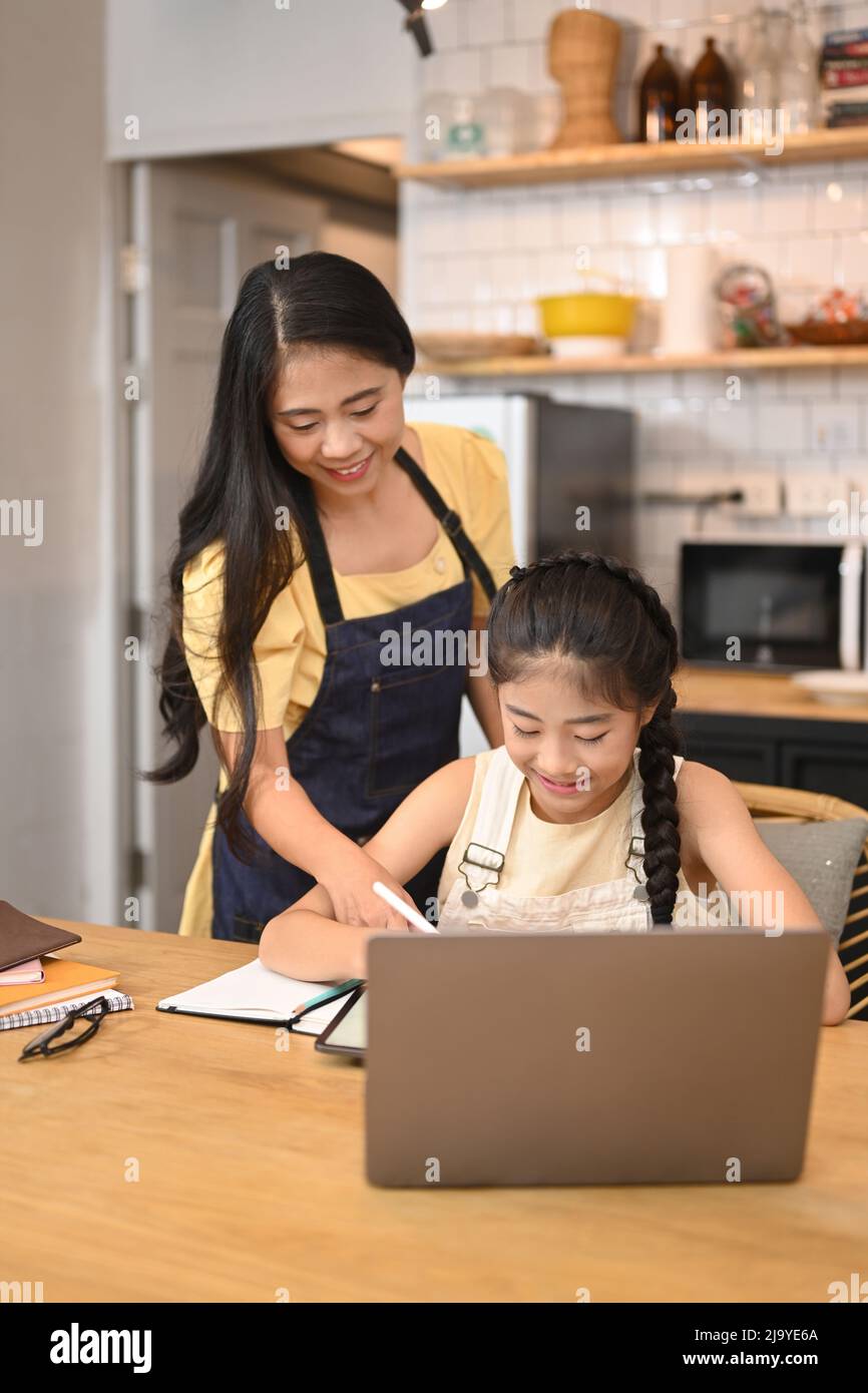 Une mère asiatique attentionnée aide sa fille à faire ses devoirs dans une table de cuisine Banque D'Images