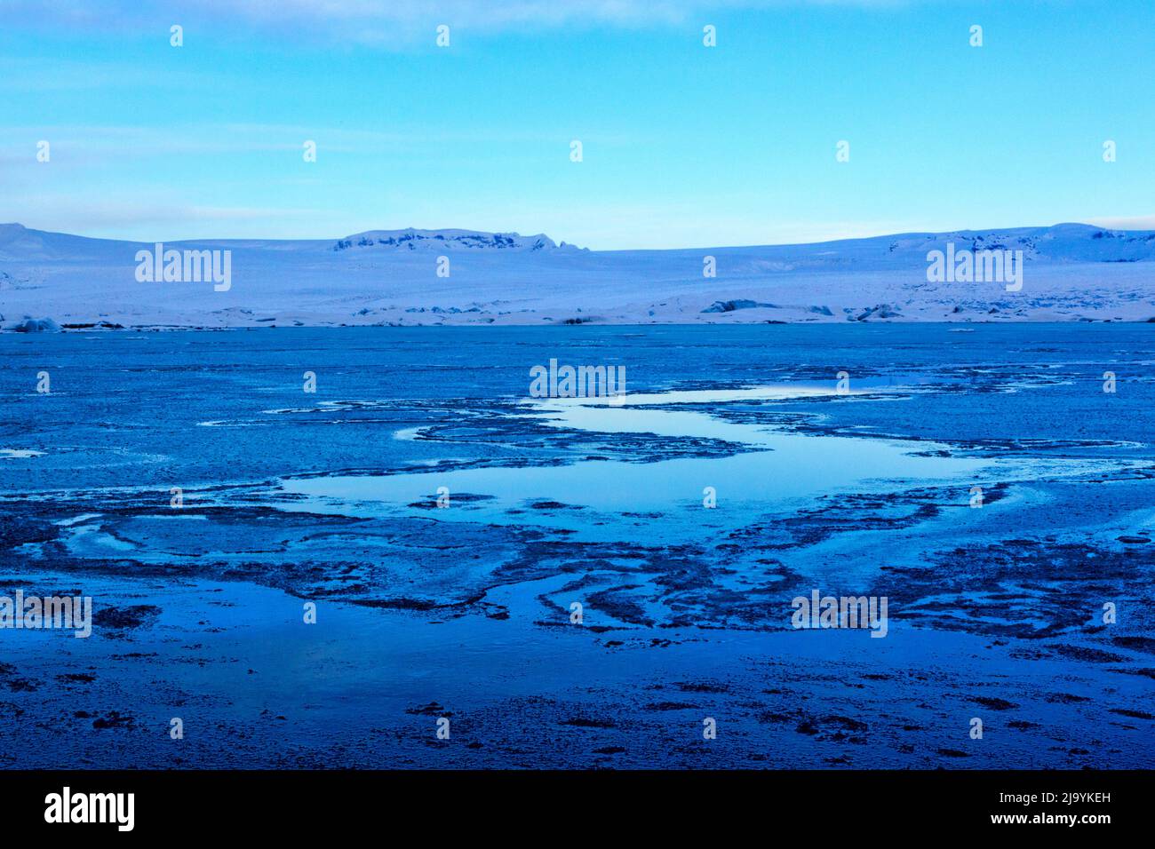 Une vue d'hiver à l'heure bleue le matin sur la lagune de l'iceberg de Jökulsarlön sans icebergs. Le lagon est recouvert d'une couche de glace fine cassée. Banque D'Images