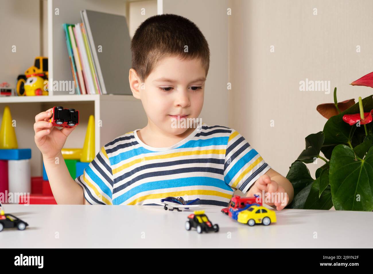 Un enfant d'âge préscolaire joue avec des voitures jouets assises à une table à la maison. Banque D'Images