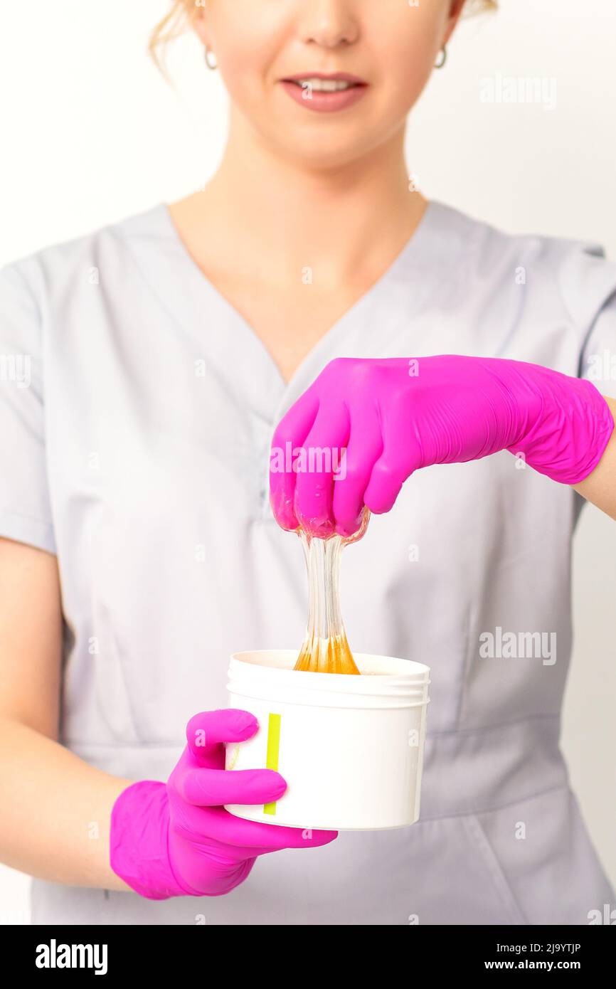 Portrait d'une esthéticienne caucasienne tenant un pot de pâte de sucre pour sugarer portant des gants roses sur fond blanc Banque D'Images