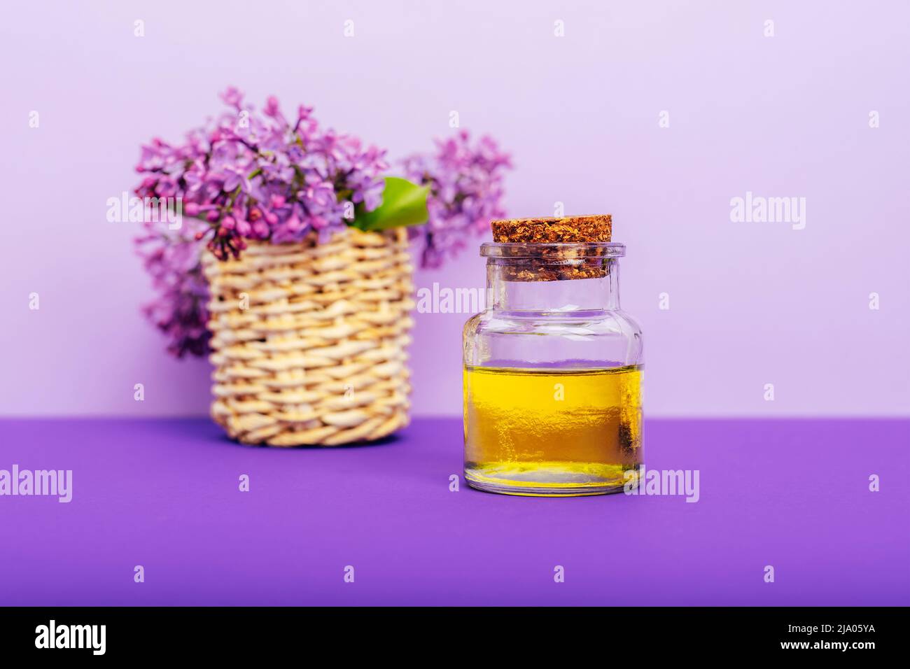 Huile cosmétique dans un pot et fleurs de lilas sur fond violet. Aromathérapie, concept de soins de la peau. Mise au point sélective. Banque D'Images