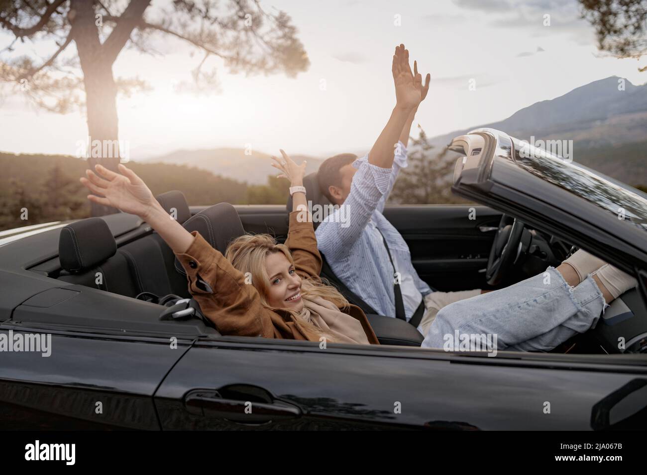 Vue latérale d'un ami joyeux et d'une petite amie assis dans une voiture convertible en montagne Banque D'Images