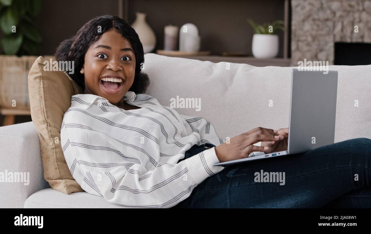 African girl étudiante femme freelancer avec ordinateur portable couché sur le canapé obtenir de bonnes nouvelles offrent positive haute marque pour le test avis de travail bonheur succès gagner Banque D'Images