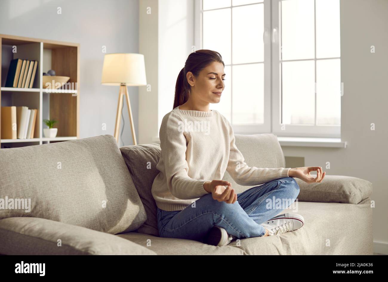 Une femme calme s'assoit sur le canapé pour pratiquer le yoga Banque D'Images