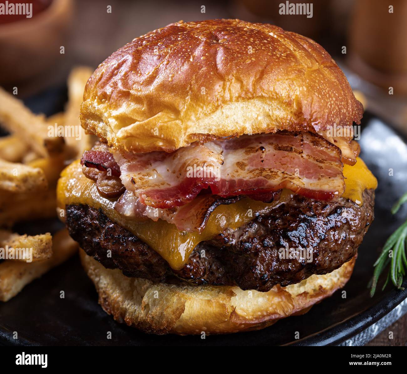 Gros plan d'un cheeseburger au bacon sur un petit pain grillé avec des frites sur une assiette Banque D'Images