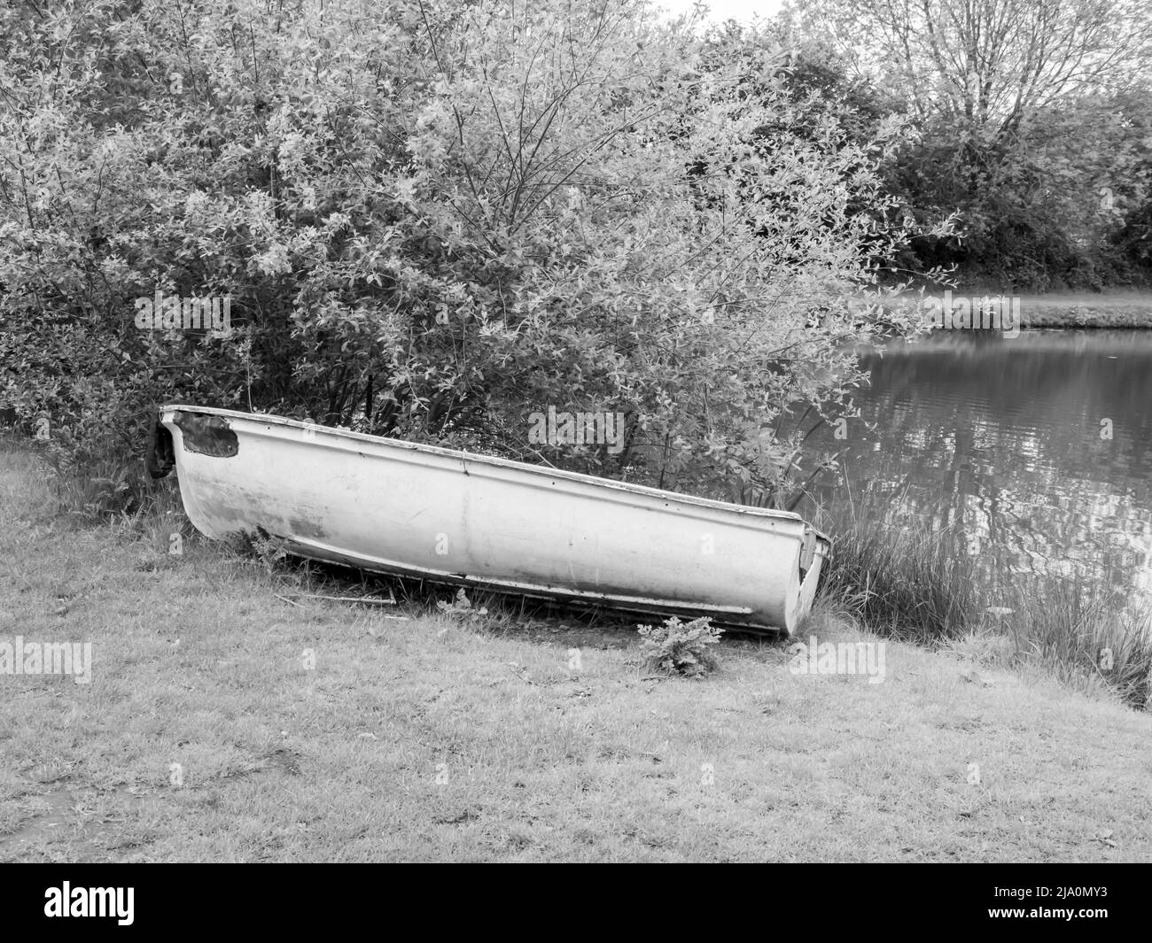 Photo de style vintage noir et blanc d'un bateau à rames abandonné sur le côté d'un étang de pêche. Banque D'Images