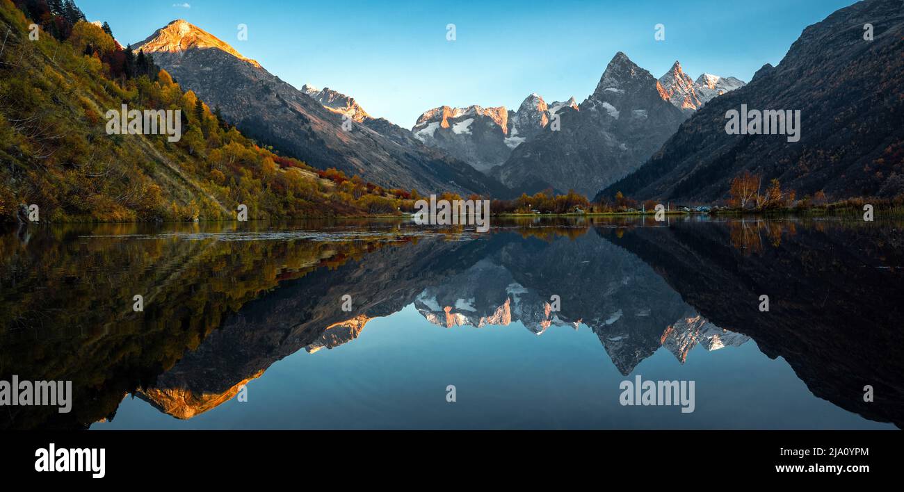 Reflet de la montagne sur le lac. Magnifique paysage avec de hautes montagnes avec des sommets illuminés et le ciel bleu. Vue panoramique sur le lac et les montagnes Banque D'Images