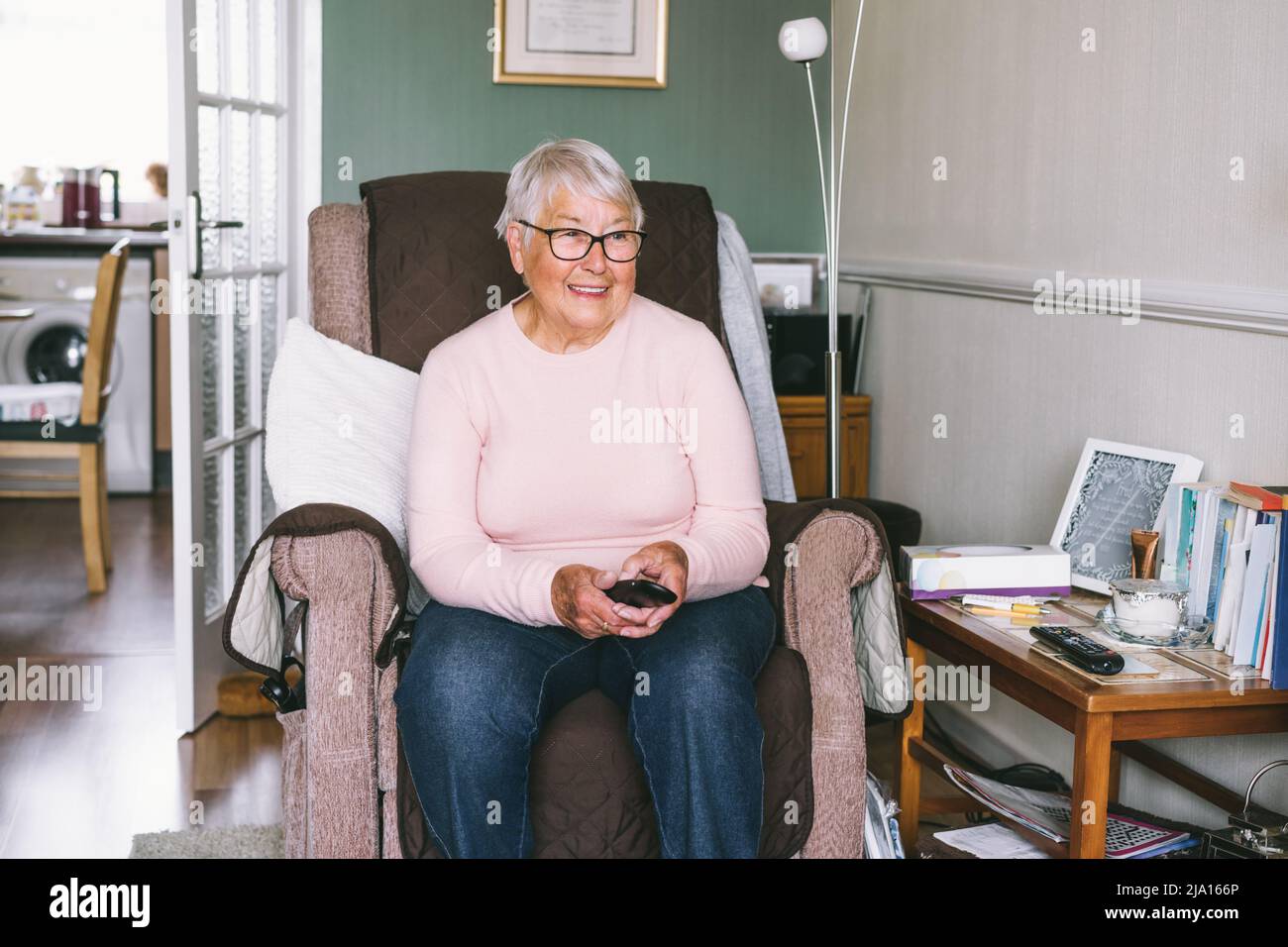 Portrait d'une femme âgée en retraite souriante dans un fauteuil confortable avec télécommande de télévision et regardant la chaîne de télévision dans le salon. Société de retraite Banque D'Images Portrait d'une femme âgée en retraite souriante dans un fauteuil confortable avec télécommande de télévision et regardant la chaîne de télévision dans le salon. Société de retraite Banque D'Images